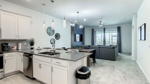 A modern kitchen with white cabinets, a central island, and a dining area with a gray sofa. - Championsgate-Free Water park/18 mins DisneyWorld (Davenport)