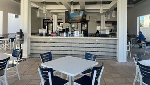An outdoor dining area with white tables and chairs, a bar counter with a television screen, and a ceiling with wooden beams and recessed lighting. - Championsgate-Free Water park/18 mins DisneyWorld (Davenport)