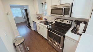 A compact kitchen with white cabinets, a stainless steel stove, a microwave, and a sink. - LIT's Palma Home - Near Beach, Downtown, Shopping, & More!! (West Palm Beach)
