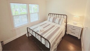 A bedroom with a bed, a nightstand, a lamp, a ceiling fan, and a window with blinds. - LIT's Palma Home - Near Beach, Downtown, Shopping, & More!! (West Palm Beach)