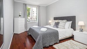 Un dormitorio moderno con una cama grande, una mesita de noche, un aparador y una ventana con cortinas.