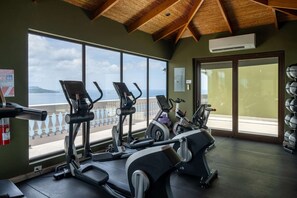 A gym with treadmills and exercise bikes, large windows with a view of the sea, and a wooden ceiling. - Flamingo Bliss: Ocean-View Condo in Luxury Complex - 360 Splendor 204 (Playa Flamingo)