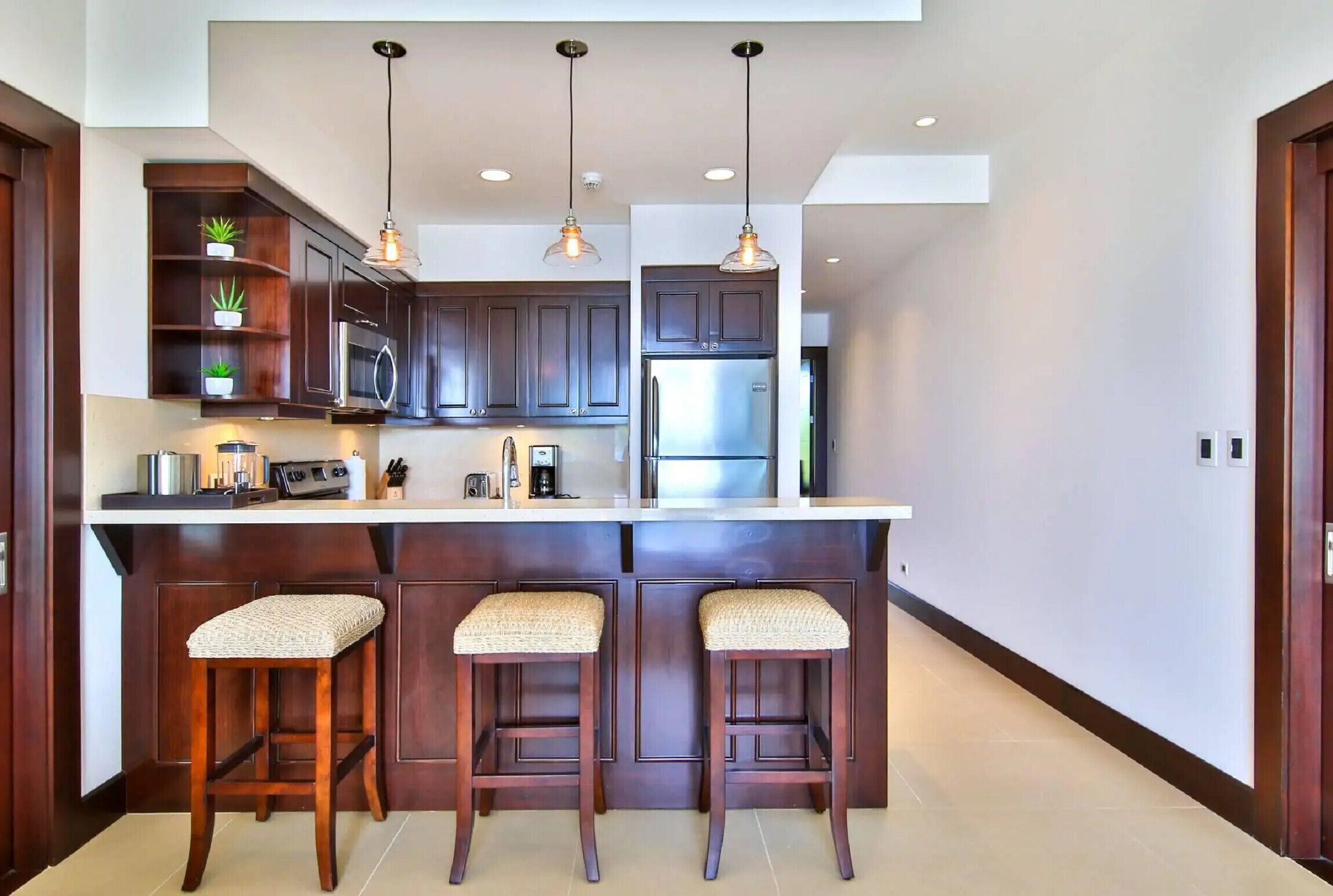 A modern kitchen with dark wood cabinets, a large island with bar stools, pendant lighting, and built-in appliances.