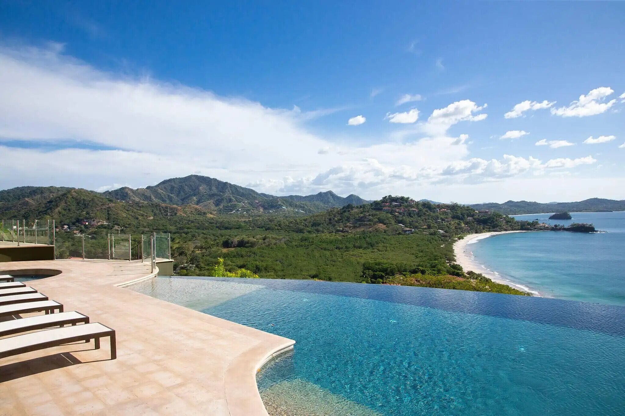 Una piscina infinita con vistas a una playa y montañas.