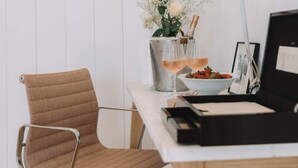 Ein Arbeitsplatz mit Stuhl, Schreibtisch, gerahmtem Bild, Schreibtischlampe, Blumen und einer Champagnerflasche.