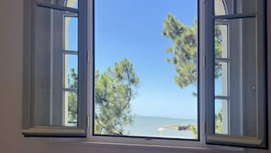 Ein Schlafzimmer mit großem Fenster und Blick auf Strand und Bäume.