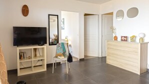 A modern living room with a flat-screen TV, a bookshelf, a chair, a dresser, and a door leading to another room. - Casa Ghju (Algajola)