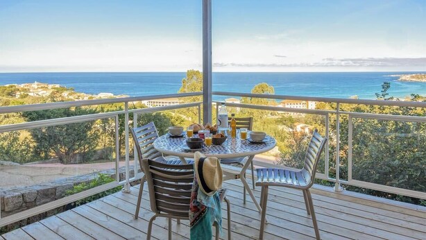 A wooden deck with a round table and chairs, overlooking a coastal landscape. - Casa Lucia (Algajola)