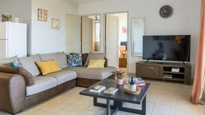 A modern living room with a sectional sofa, a coffee table, a flat-screen TV, and a clock on the wall. - Casa Lucia (Algajola)