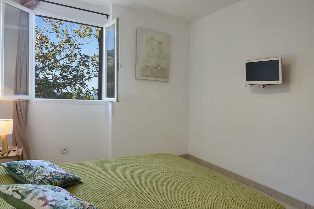 A room with a bed, a window, a wall-mounted TV, and a painting.