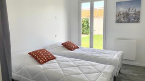 A bedroom with two beds, white bedding, and a view of a garden through a sliding door. - Villa SAINT MART (11 rue de la Réunion, Saint Martin) (Saint-Martin-de-Ré)