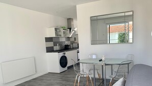 A modern kitchen with a washing machine, a dining area with a glass table and chairs, and a large window. - Villa SAINT MART (11 rue de la Réunion, Saint Martin) (Saint-Martin-de-Ré)