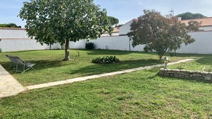 A well-maintained backyard with a lawn, two trees, a stone wall, and a metal chair. - Villa SAINT MART (11 rue de la Réunion, Saint Martin) (Saint-Martin-de-Ré)