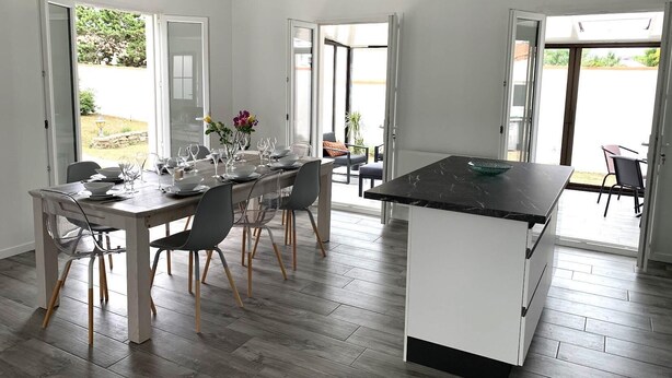 A modern kitchen with a dining area, large windows, and a view of the outdoors. - Villa SAINT MART (11 rue de la Réunion, Saint Martin) (Saint-Martin-de-Ré)