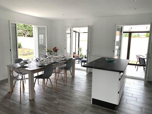 A modern kitchen with a dining area, large windows, and a view of the outdoors.