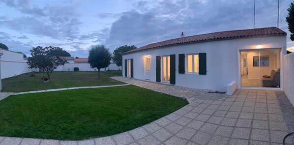 A modern house with a tiled roof, a well-maintained lawn, and a paved driveway leading to a glass door entrance.