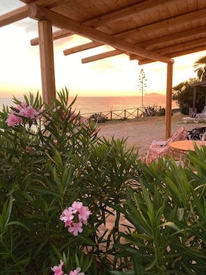 Una pérgola de madera con vista a la playa y al atardecer.