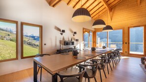 Un vaste espace dédié à la salle à manger, avec une longue table en bois, des chaises noires et des luminaires suspendus.