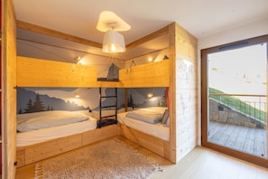 A room with two bunk beds, a wooden ceiling, a large window, and a view of a balcony.