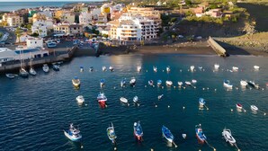 Un pueblo costero con edificios, barcos y montañas al fondo.