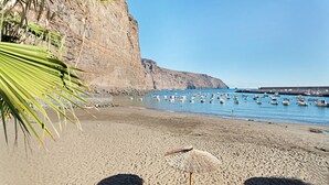 Una playa con barcos, un acantilado y un paraguas de paja.