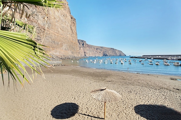 Ein Strand mit Booten, einer Klippe und einem Reetdachschirm.