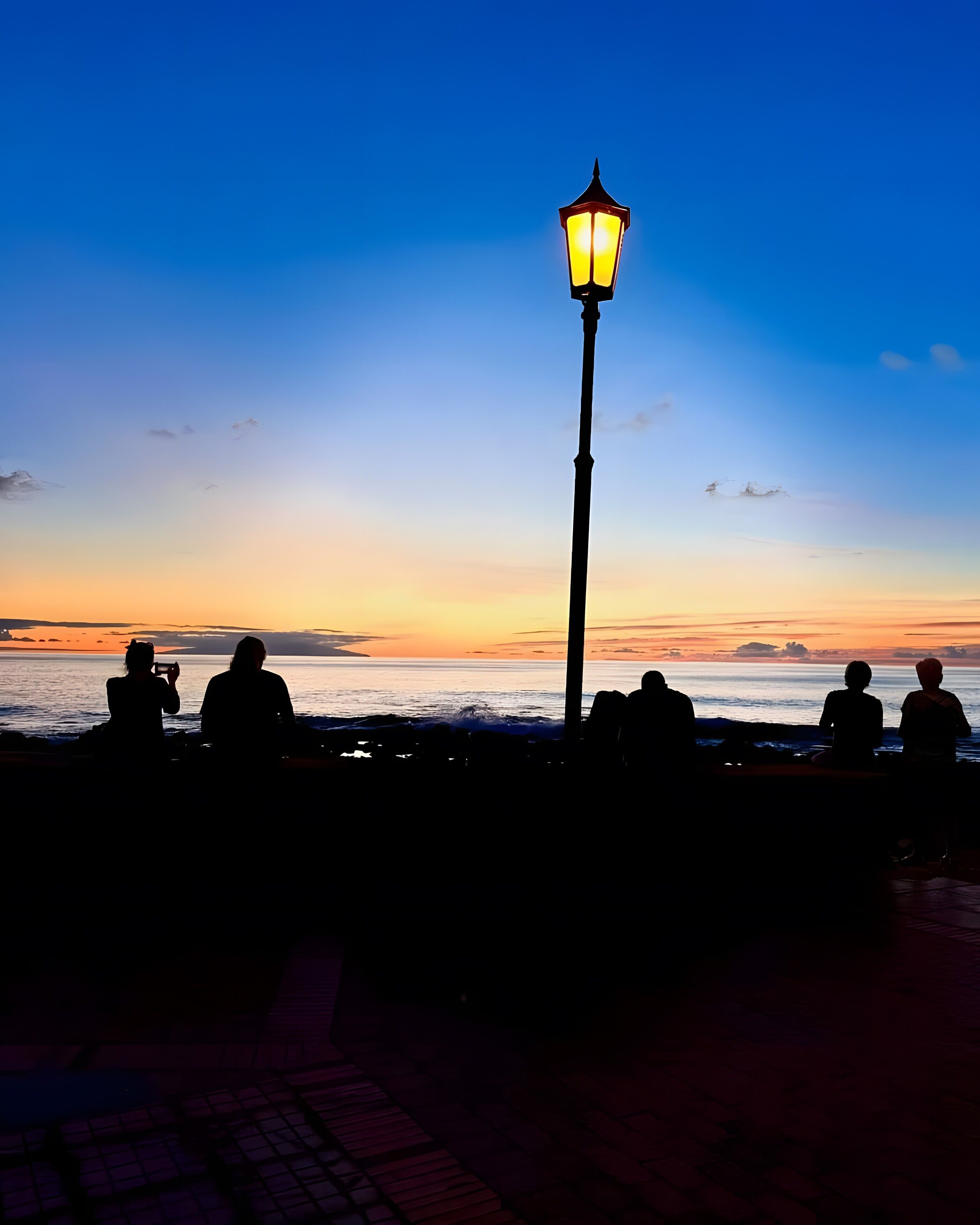 A sunset view with silhouettes of people and a street lamp.