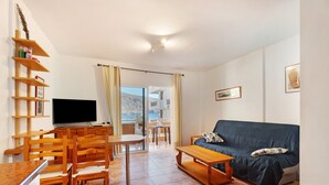 Una sala de estar con sofá, mesa de centro, televisor, sillas de madera y mesa de comedor.