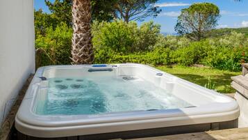 Un bain à remous dans un jardin, avec un mur blanc, un palmier et une végétation luxuriante.