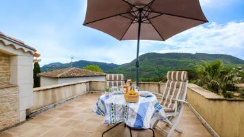 Une terrasse avec une table dressée pour deux personnes, un grand parasol et une vue sur des collines verdoyantes.