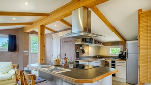 A modern kitchen with a central island, wooden beams, and a view of the outdoors. - Loft 50m² au calme avec vue splendide piscine (Les Adrets-de-l'Estérel)