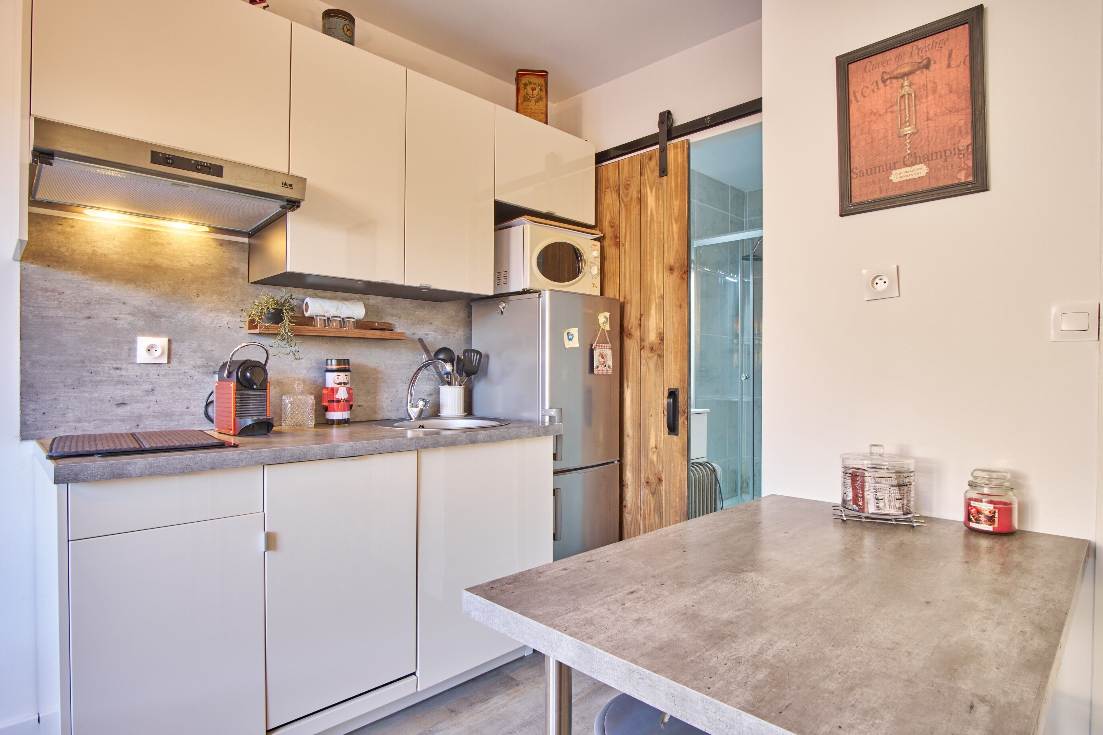Cucina moderna con mobili bianchi, frigorifero in acciaio inossidabile, forno a microonde e una porta in legno.