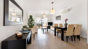 A modern living room with a dining area, a large mirror, and a television. - Chez Hélène et Paulo Apartment with Shared Pool, Wi-Fi, and Air Conditioning (Lagos)