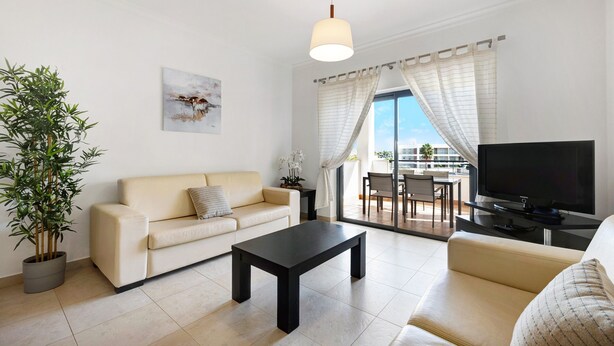 A modern living room with a sofa, a coffee table, a TV, a potted plant, and a painting on the wall. - Chez Hélène et Paulo Apartment with Shared Pool, Wi-Fi, and Air Conditioning (Lagos)