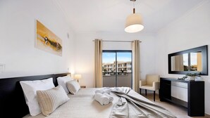 A hotel room with a bed, a desk, a chair, a large window, and a painting on the wall. - Chez Hélène et Paulo Apartment with Shared Pool, Wi-Fi, and Air Conditioning (Lagos)