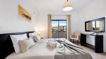 A hotel room with a bed, a desk, a chair, a large window, and a painting on the wall.