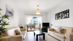 A living room with a sofa, coffee table, TV, and artwork. - Chez Hélène et Paulo Apartment with Shared Pool, Wi-Fi, and Air Conditioning (Lagos)