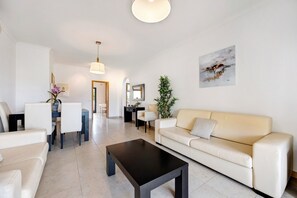 A modern living room with a sofa, coffee table, dining area, and a painting on the wall. - Chez Hélène et Paulo Apartment with Shared Pool, Wi-Fi, and Air Conditioning (Lagos)