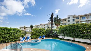 A swimming pool with lounge chairs, a hot tub, and a view of a multi-story building with balconies. - Chez Hélène et Paulo Apartment with Shared Pool, Wi-Fi, and Air Conditioning (Lagos)