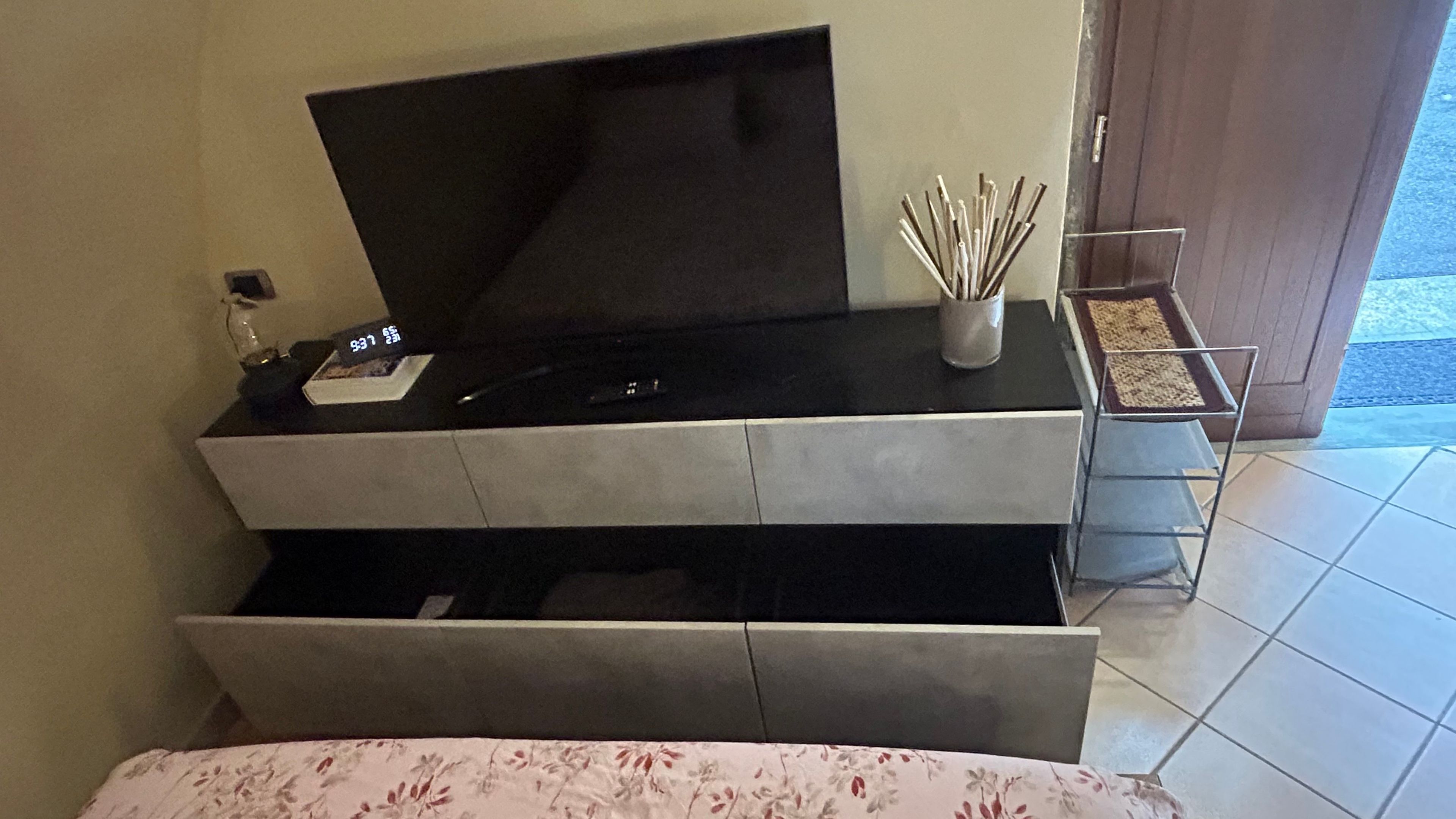 A modern living room with a flat-screen TV on a black stand, a small table with a candle holder, and a patterned sofa.