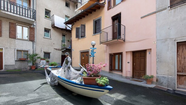 A narrow street with a boat parked in front of a building with balconies and potted plants.
