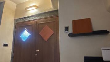 A room with a wooden door, a light fixture above it, and a wall-mounted shelf with a small item on it.
