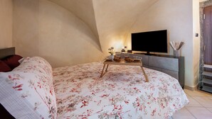 A bedroom with a curved ceiling, a bed with floral bedding, a bedside table with decorative items, a flat-screen TV, and a wardrobe.