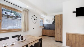 A modern kitchen with wooden cabinets, a dining area with a wooden table and chairs, and a large wall clock. - Apartment 'Chalet Snowlake Neve' with Mountain View, Private Garden and Wi-Fi (Livigno)