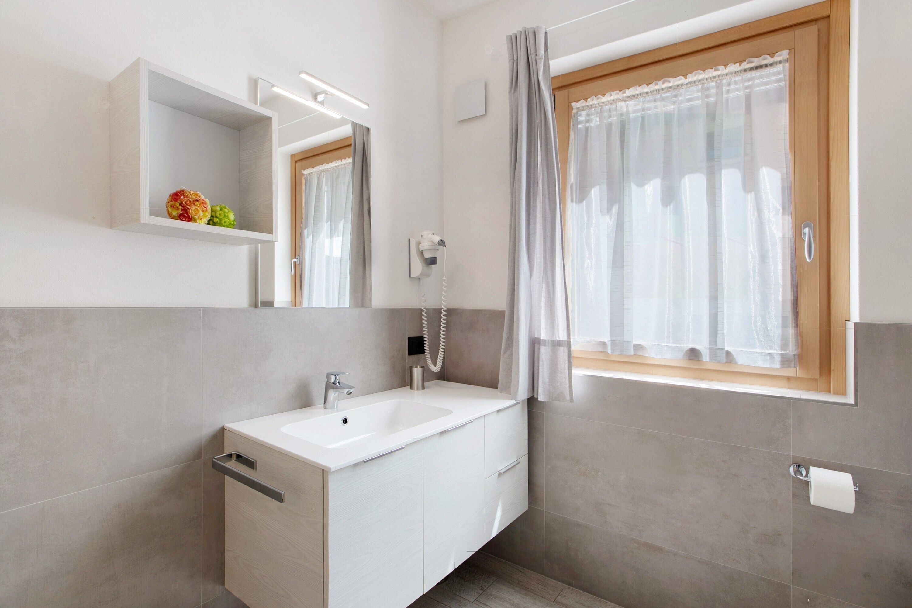 Un bagno moderno con lavandino bianco, specchio e tenda da doccia.