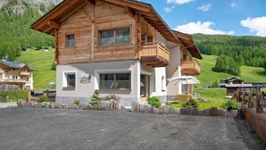 A two-story wooden chalet with a balcony, a small porch, and a view of a green valley. - Apartment 'Chalet Snowlake Neve' with Mountain View, Private Garden and Wi-Fi (Livigno)