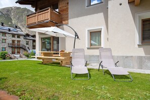 Un chalet doté d’une terrasse en bois, de deux chaises longues, d’une table et d’un espace salon couvert avec un parasol.