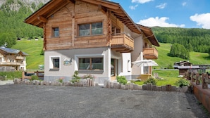 Een houten chalet met twee verdiepingen, een balkon, een klein terras en uitzicht op een groene vallei.