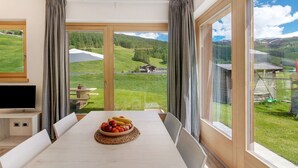 Een eetruimte met een tafel gedekt voor twee personen, een schaal fruit en een televisie op een standaard.