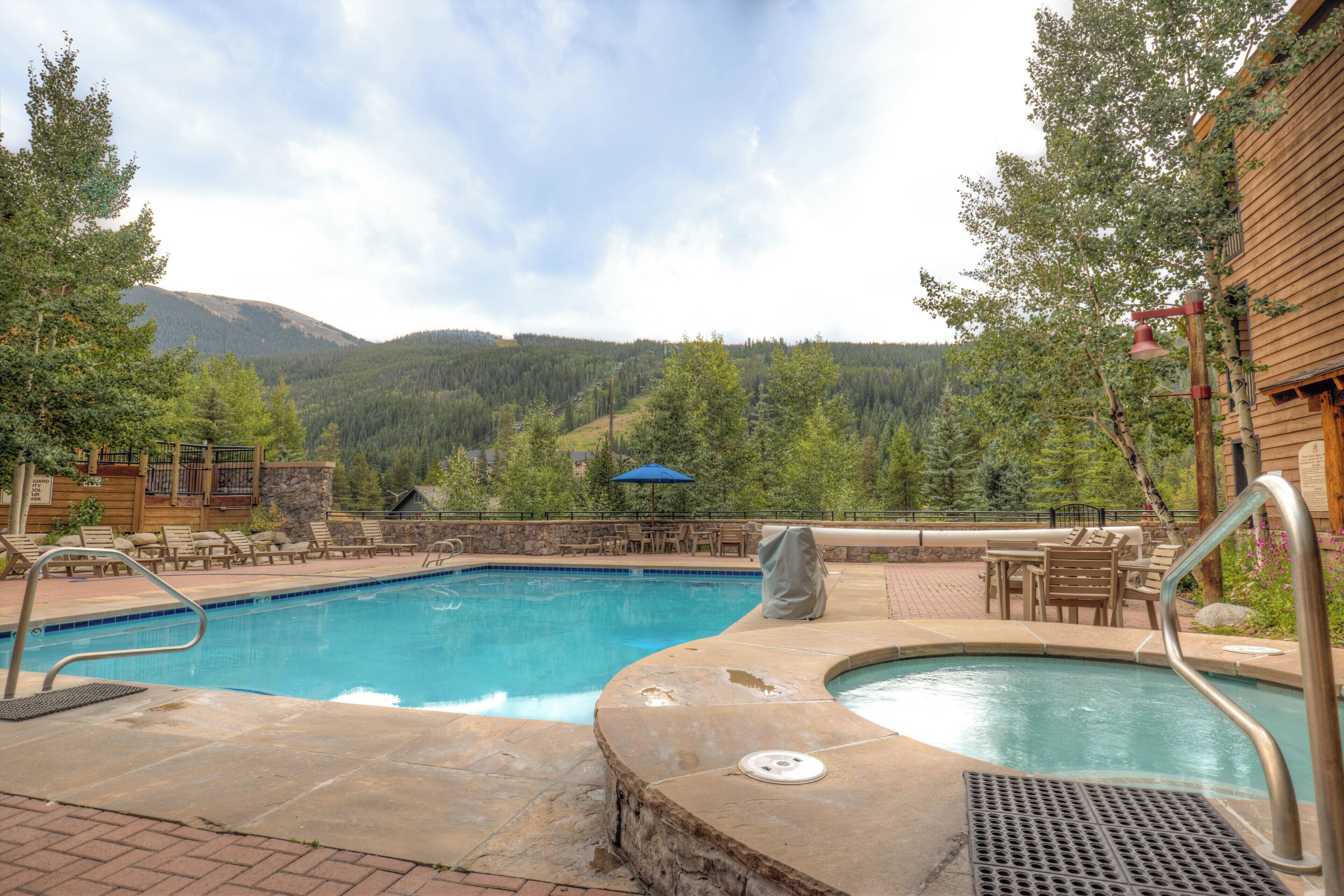 A swimming pool with a hot tub, lounge chairs, and a view of a forested mountain range.